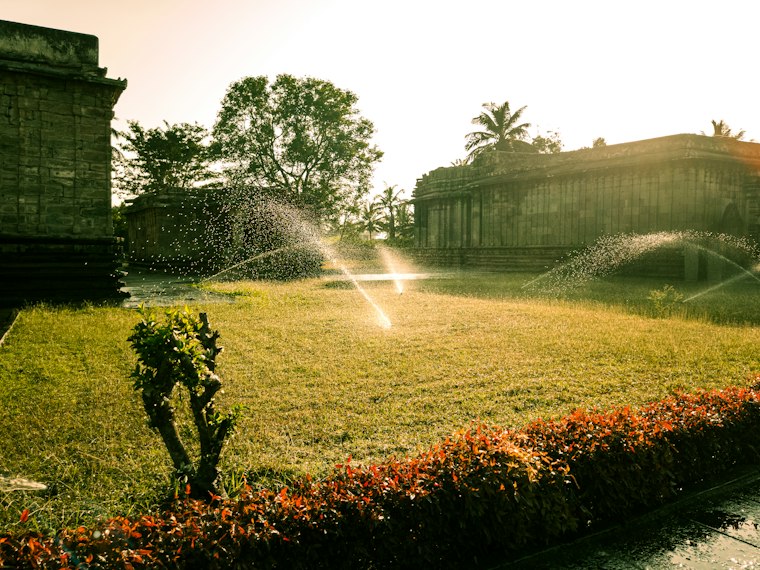 Aspersores de riego automático regando el césped de un jardín al atardecer